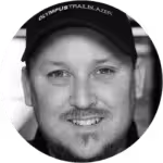 Smiling man with light facial hair wearing a dark cap in a circular frame.