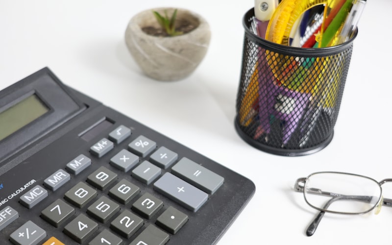 Calculatrice, lunettes et stylos sur un bureau blanc pour calculer le prix d'incorporation au Québec