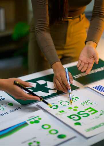 Two people pointing with pens at printed materials on recycling and environmental themes on a table.