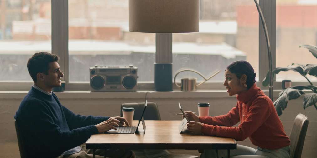 Two people collaborating at a workspace with open laptops and notes