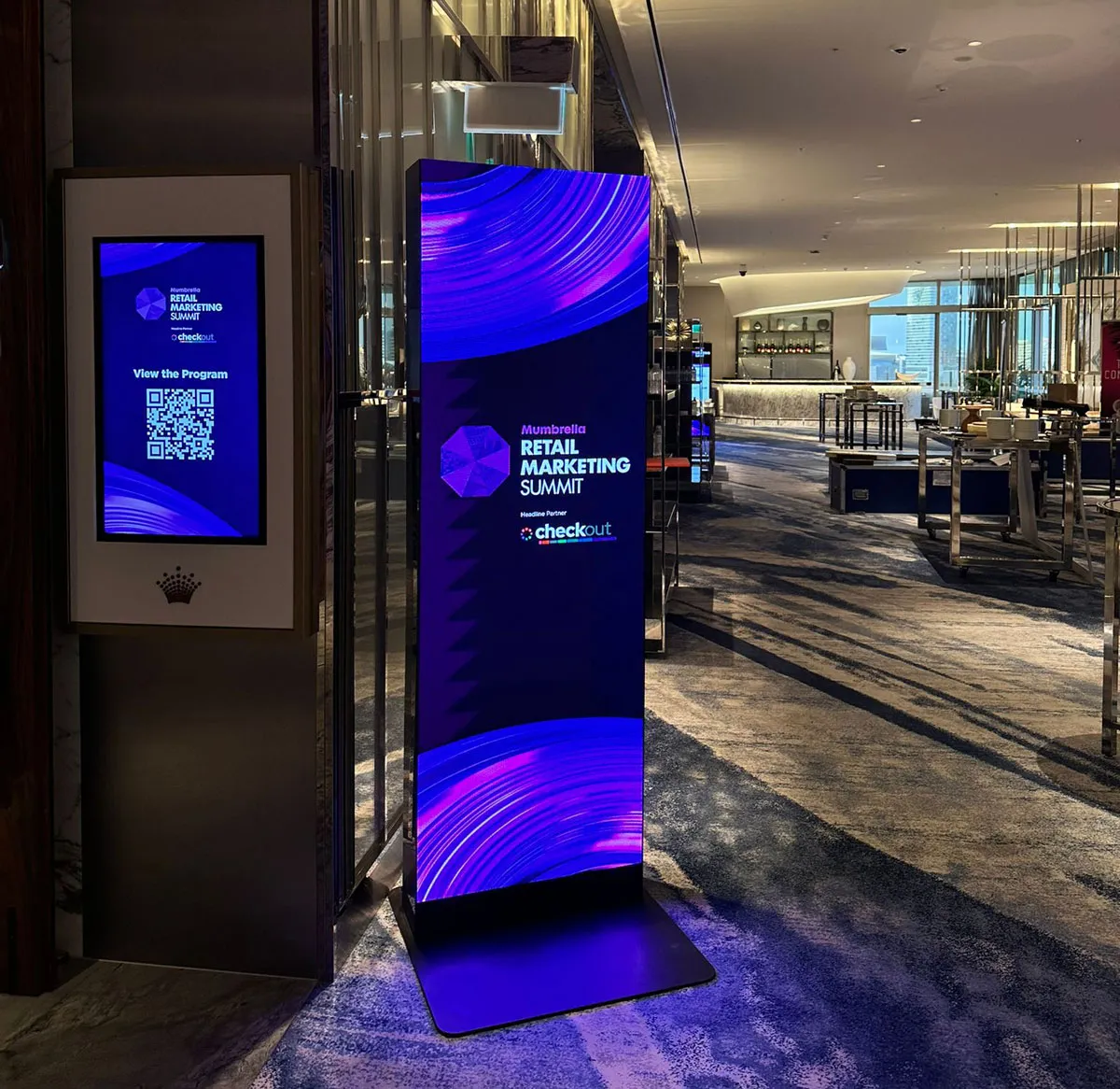 Digital signage in a modern indoor space displaying 'Mumbrella Retail Marketing Summit' with a QR code to view the program.