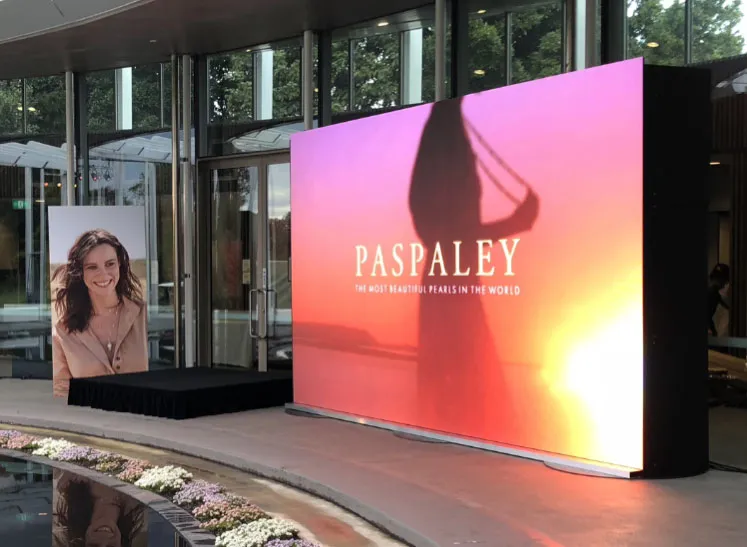 Large outdoor LED screen displaying 'PASPALEY' and 'The Most Beautiful Pearls in the World' with a silhouette of a woman against a sunset background near a building entrance.