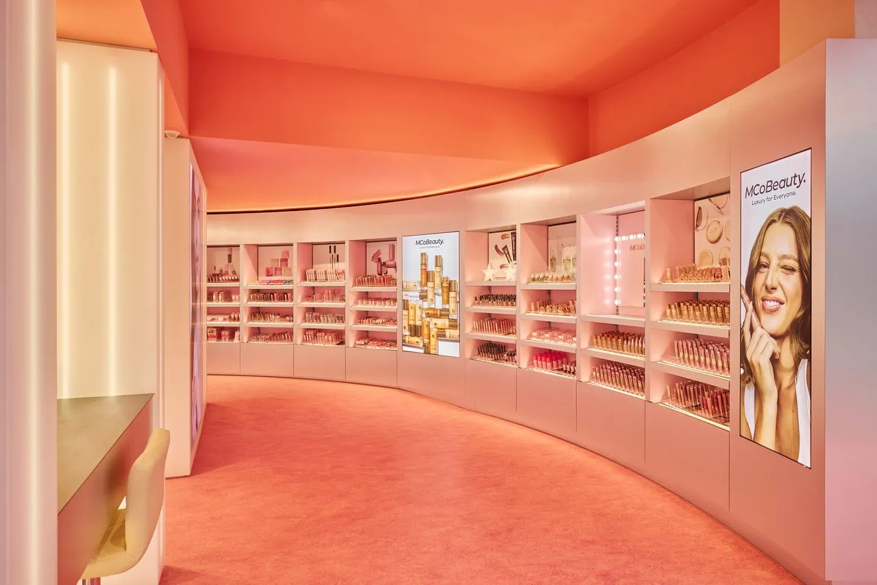 Curved pink-themed beauty store interior with shelves displaying makeup products and illuminated advertising screens.
