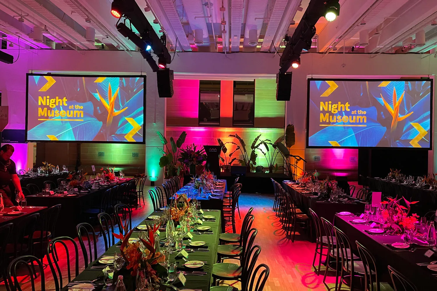 Colorfully lit event venue set for Night at the Museum dinner with floral centerpieces and rows of chairs.