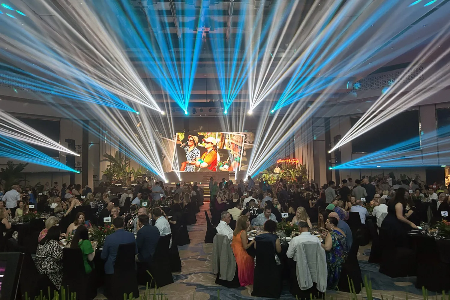 Gala dinner event with guests seated at round tables under blue and white stage lights.