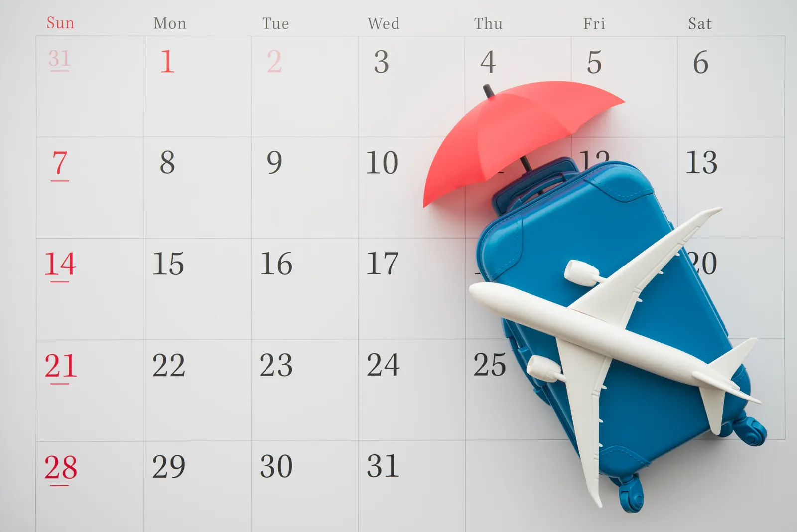 Picture of a plane model with a luggage and umbrella on top of a calendar suggesting holliday booking