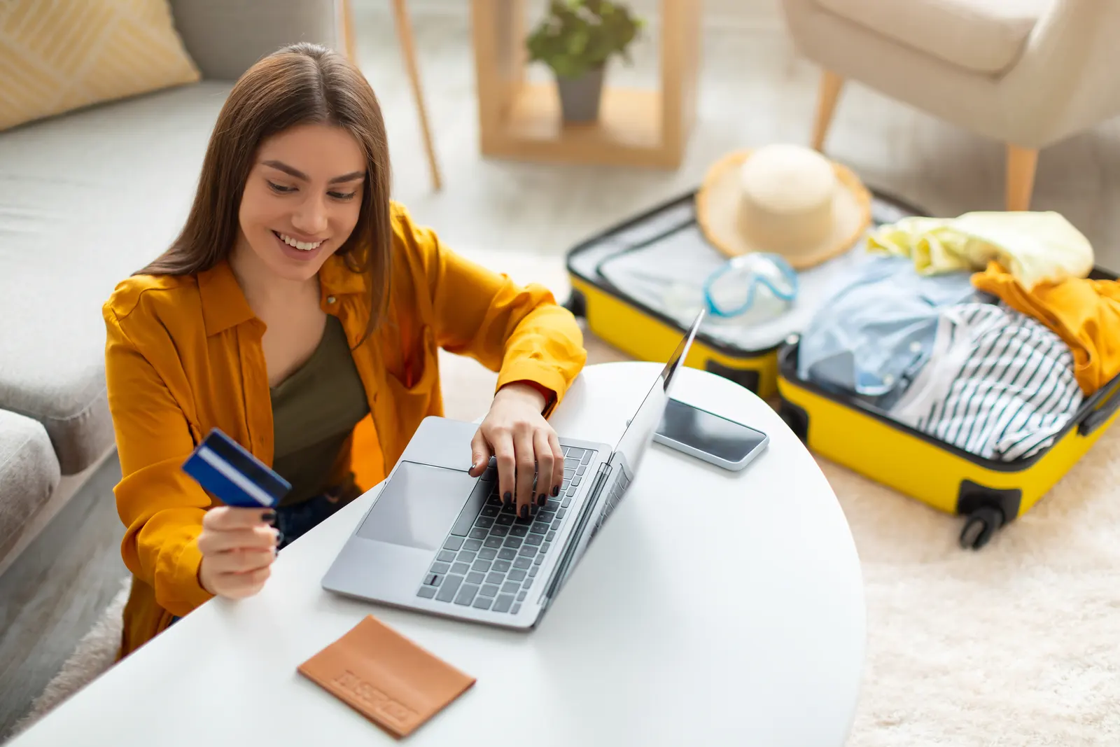 Picture of a woman using the laptop and ready to pay on the last minute for her next holiday vacation while the carry on bag is still open.