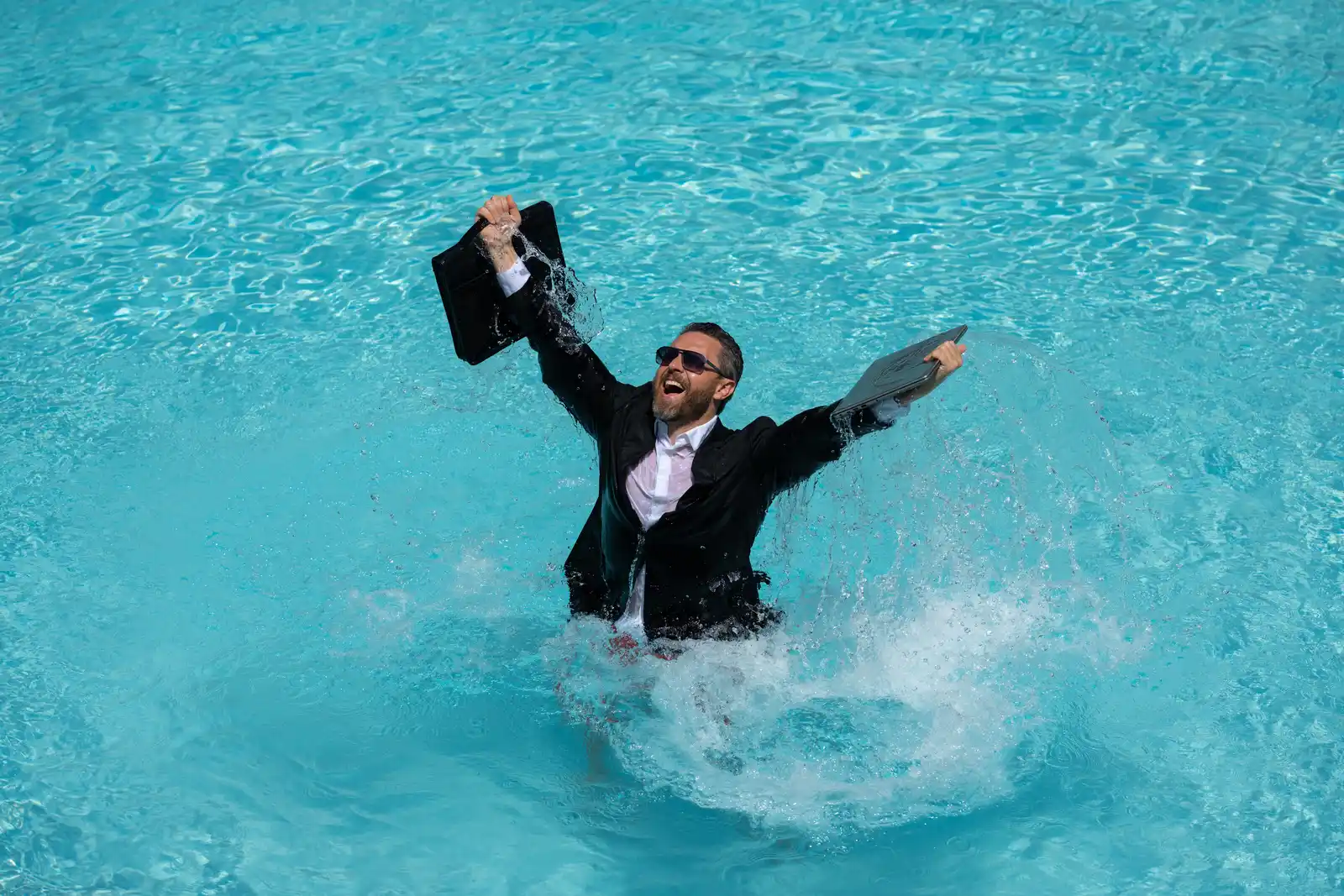 Picture of a man dressed in business clothes, more specifically a suit having the laptop with him while he is in the pool. Describing that he is not able to disconnect from work even when he is on holiday.