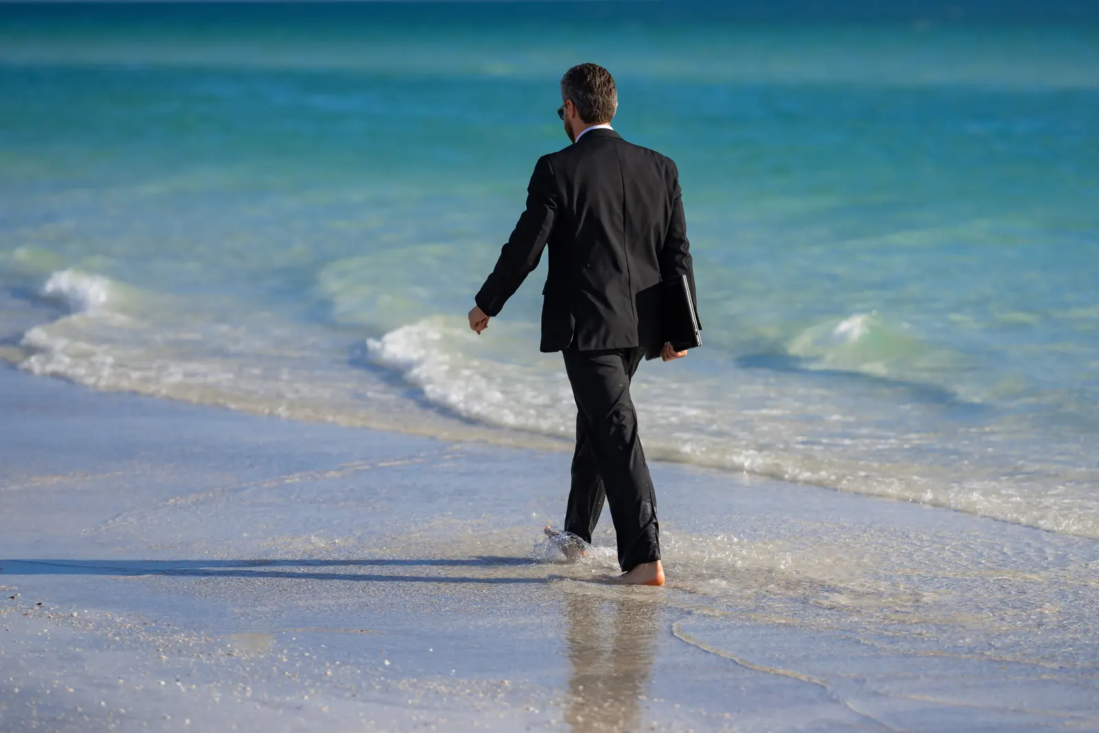 Picture of a man in a suit holding a set of documents walking casually on the beach