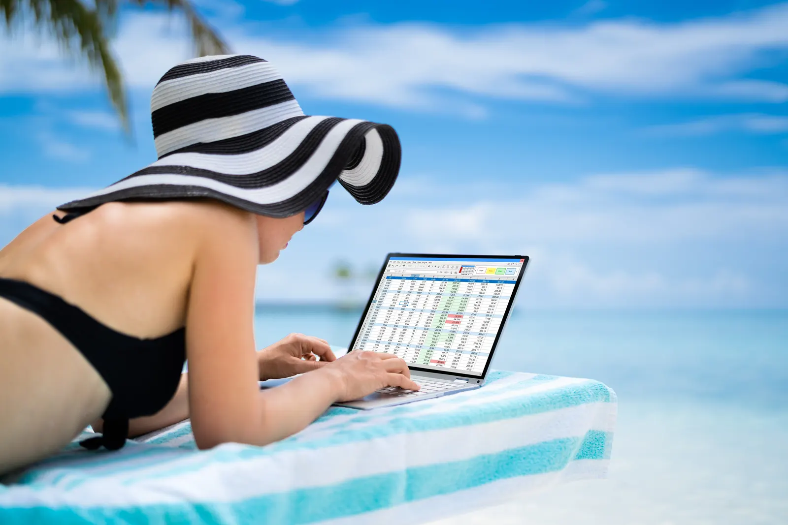 Picture of a woman working on a laptop while on the beach on holiday followiong a strict routine.