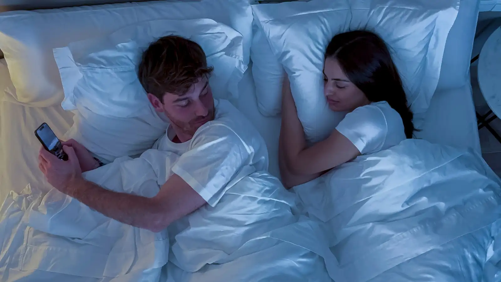 Picture of a man while in bed with his partner texting secretly to someone else.