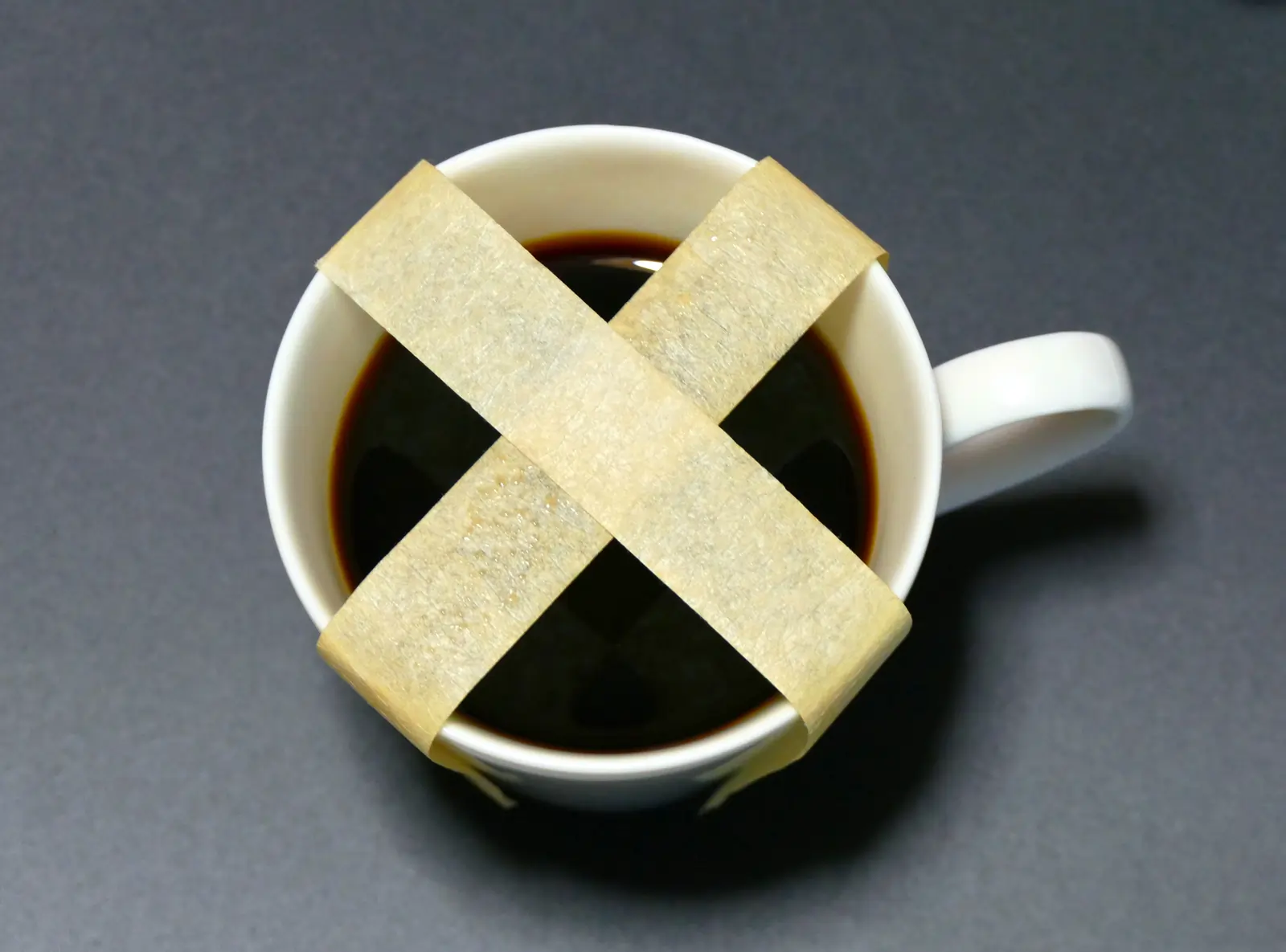 Picture of a cup of coffee with tape on top in a cross shape, suggesting a no caffeine message.