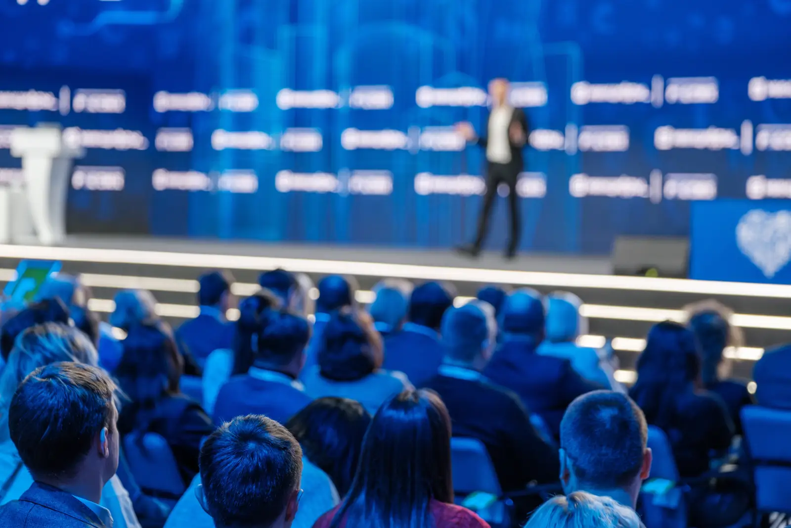 Artistic blurry picture of a successful but struggling entrepreneur giving a speech on the stage in front of an audience.
