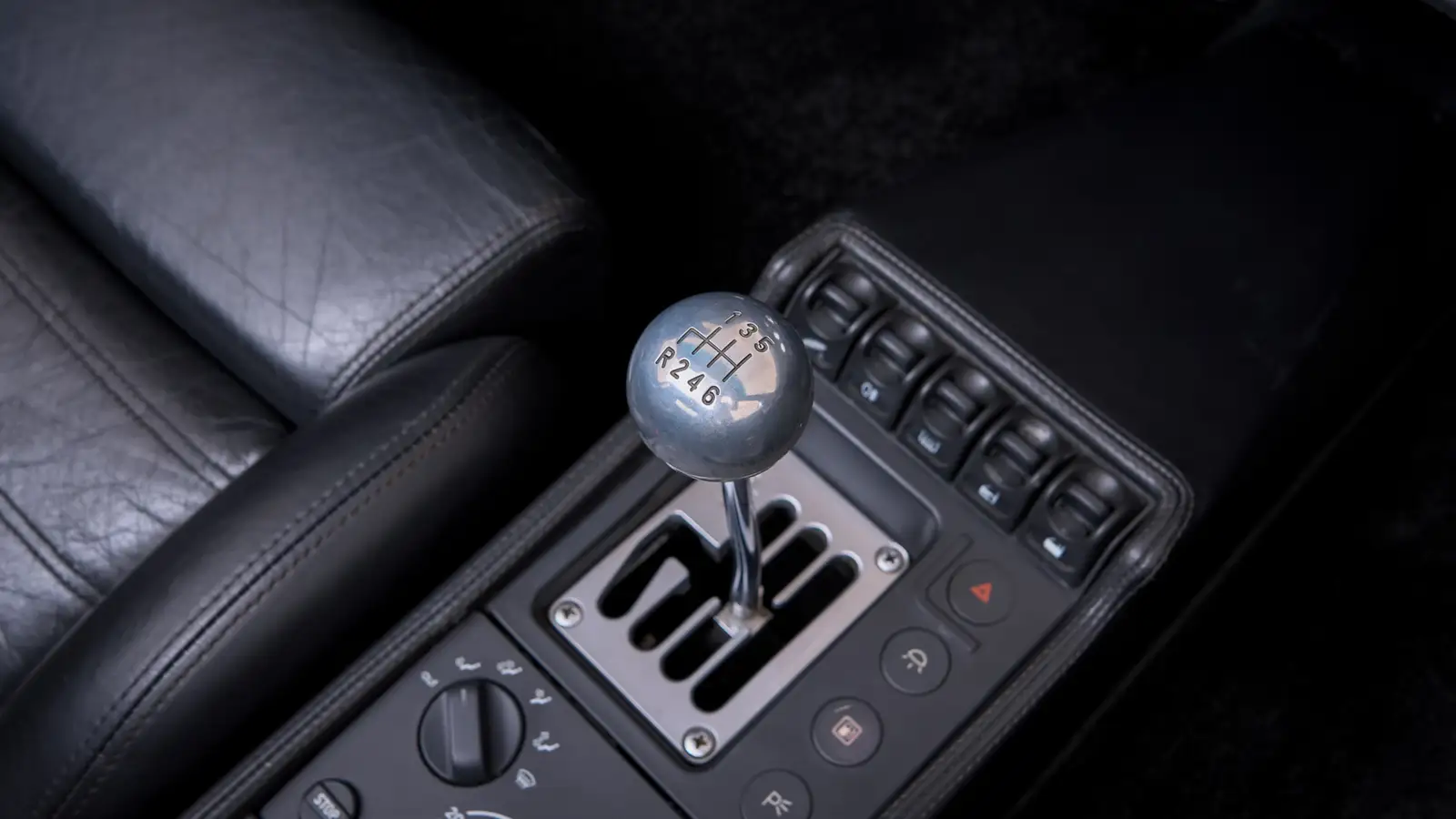 Picture of the stick of a manual gated gearbox in a sports car suggesting analog control and fewer distractions. 