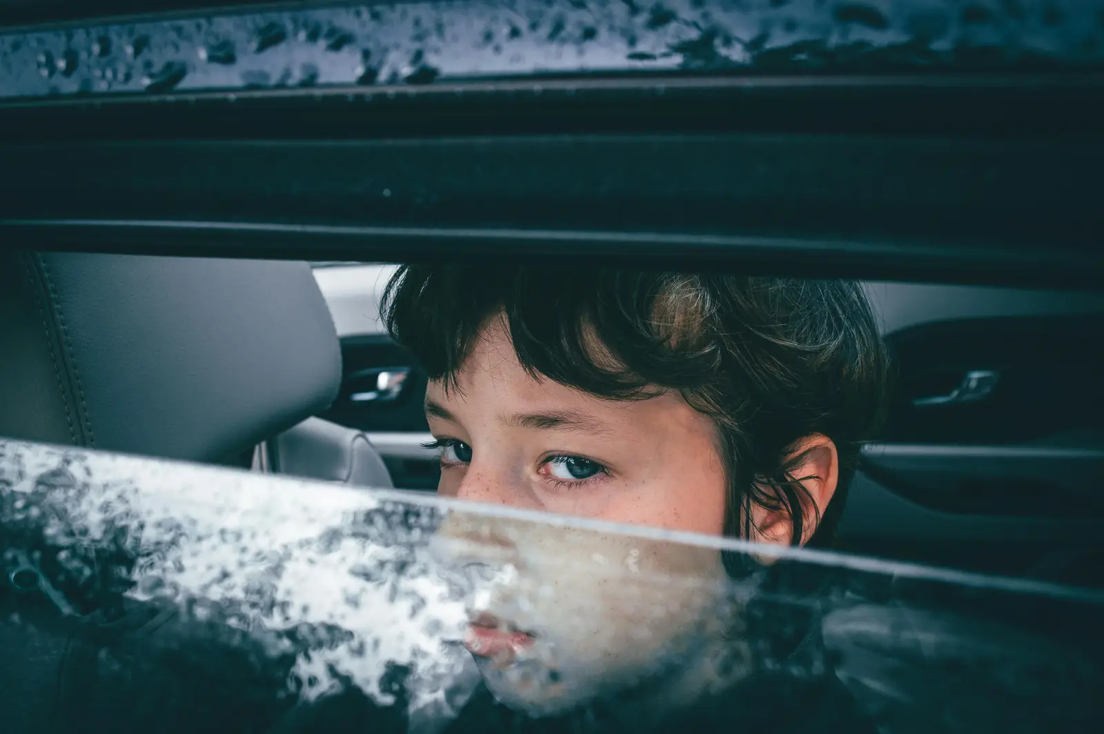 pictture of a child looking on the car window, half o[pen where you can see only their eyes. picture taken likely when going to school.