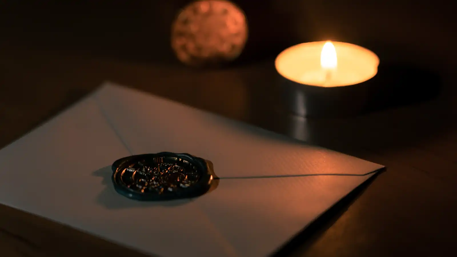 picture of a sealed envelope on the desk in a moody dark environment lighten by a candlelight. 