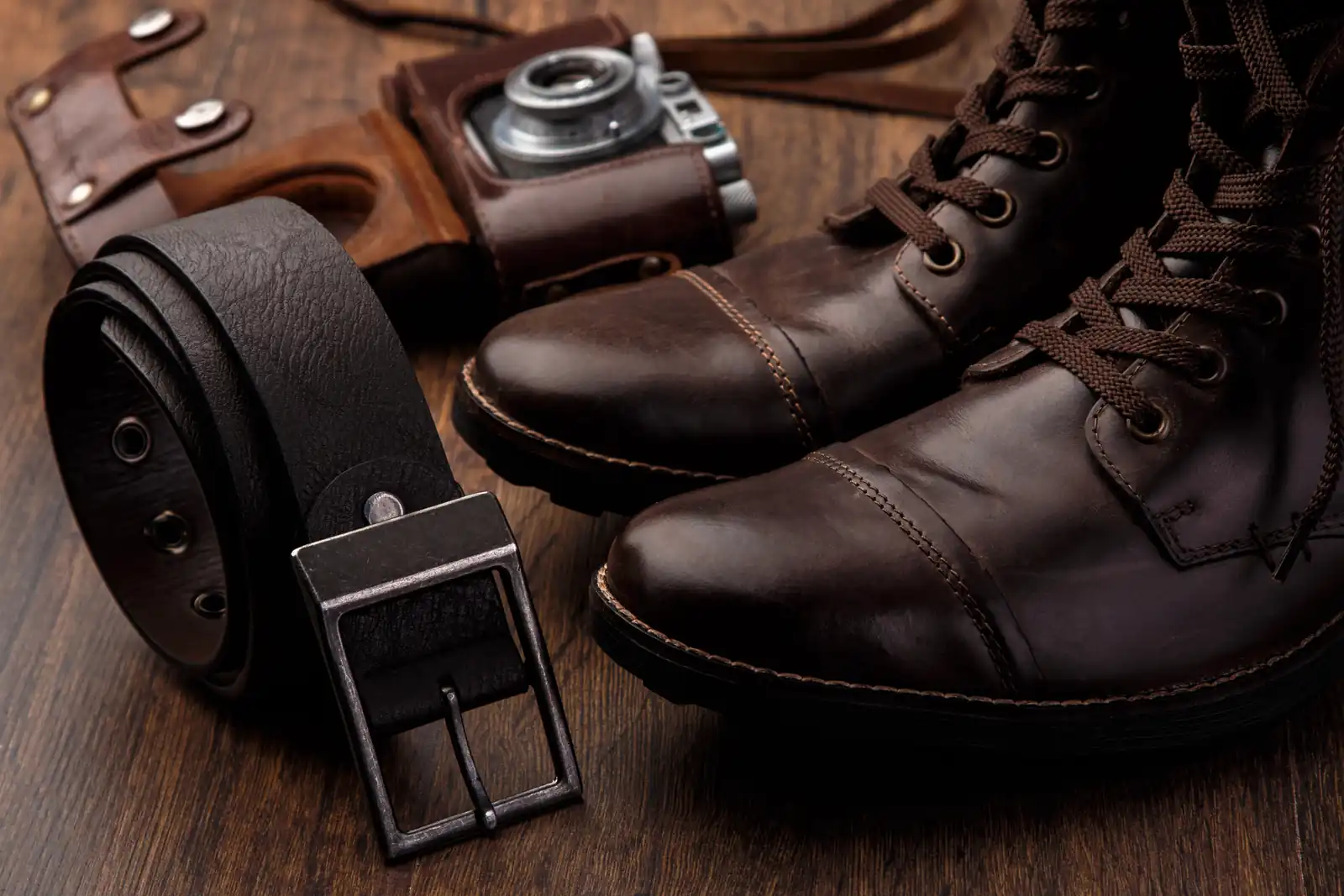 Picture of a nice quality pair of boots alongside with a quality belt and a classic rangefinder camera. 