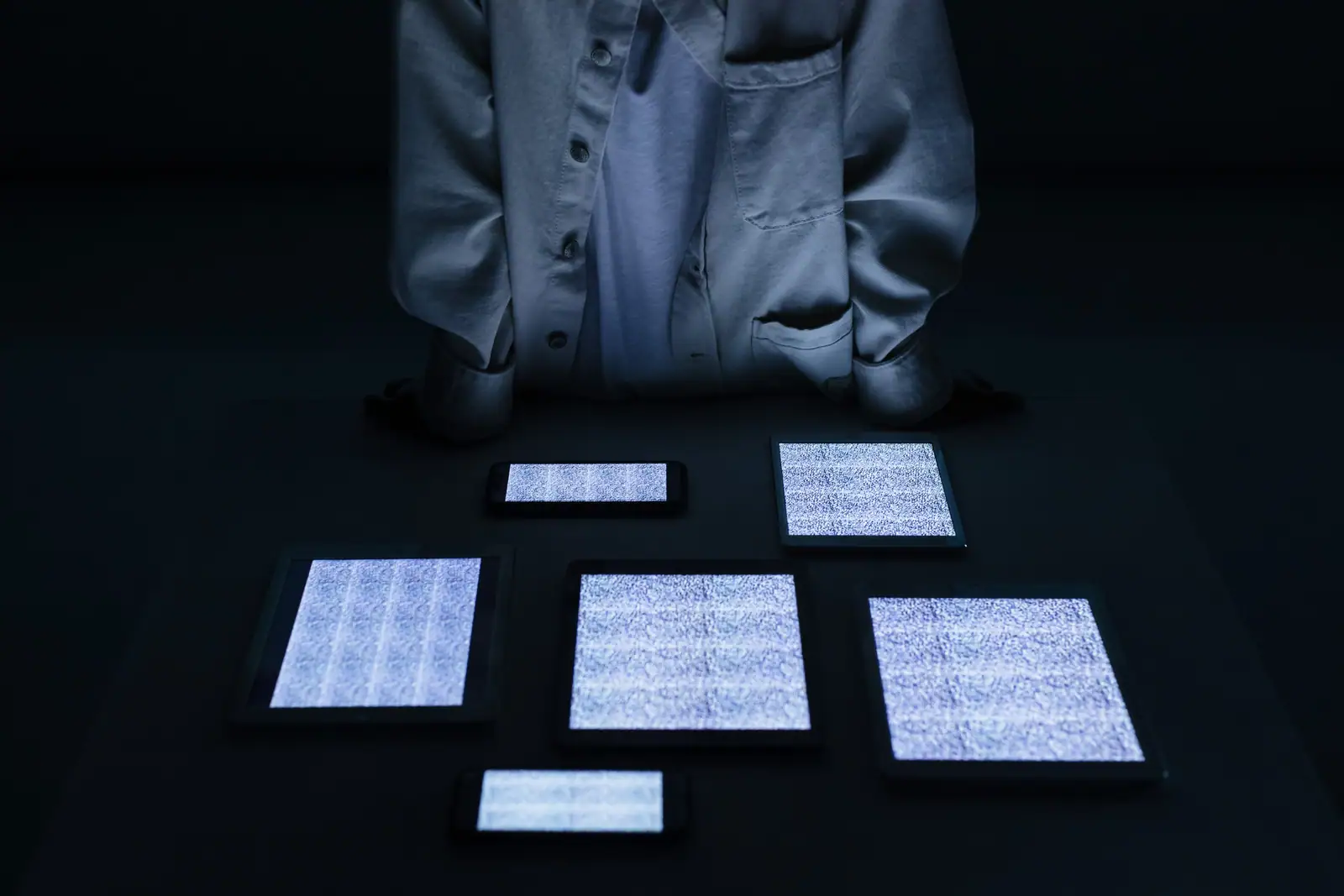 Picture of a human sitting in front of tech devices with a blank screen.