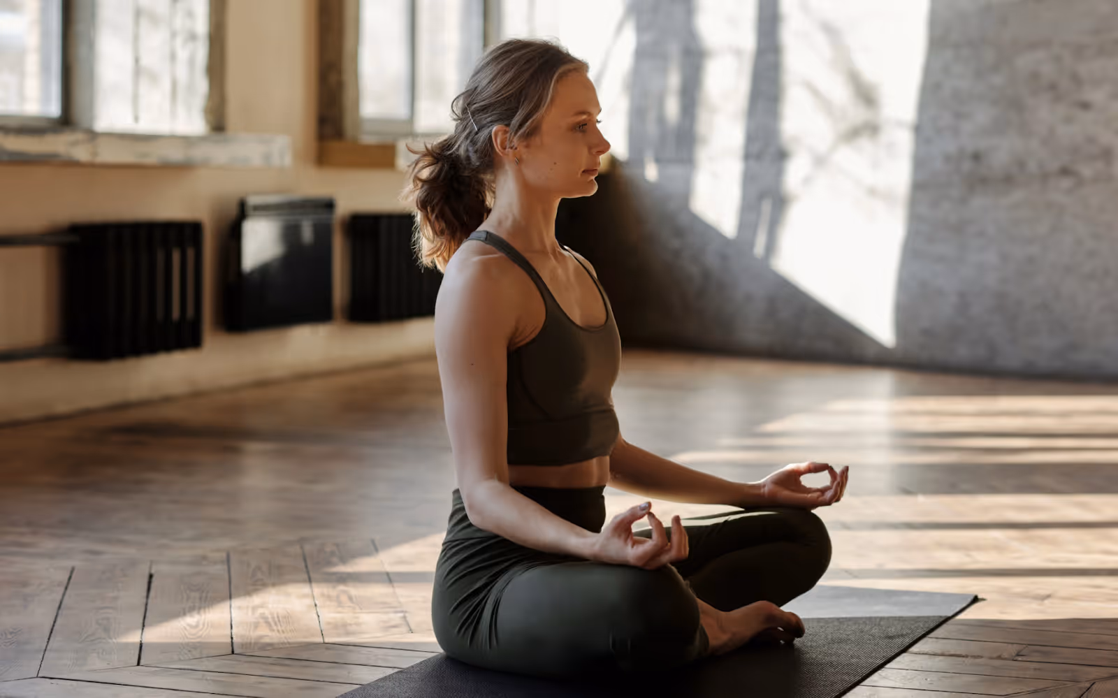 Person sitting cross-legged on a yoga mat practicing meditation in a sunlit room to support mental well-being