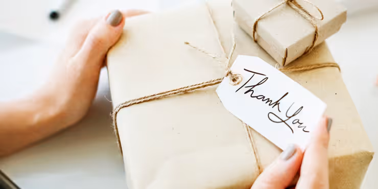 Close-up of hands holding a wrapped gift with a thank you note, symbolizing appreciation and gratitude in the workplace