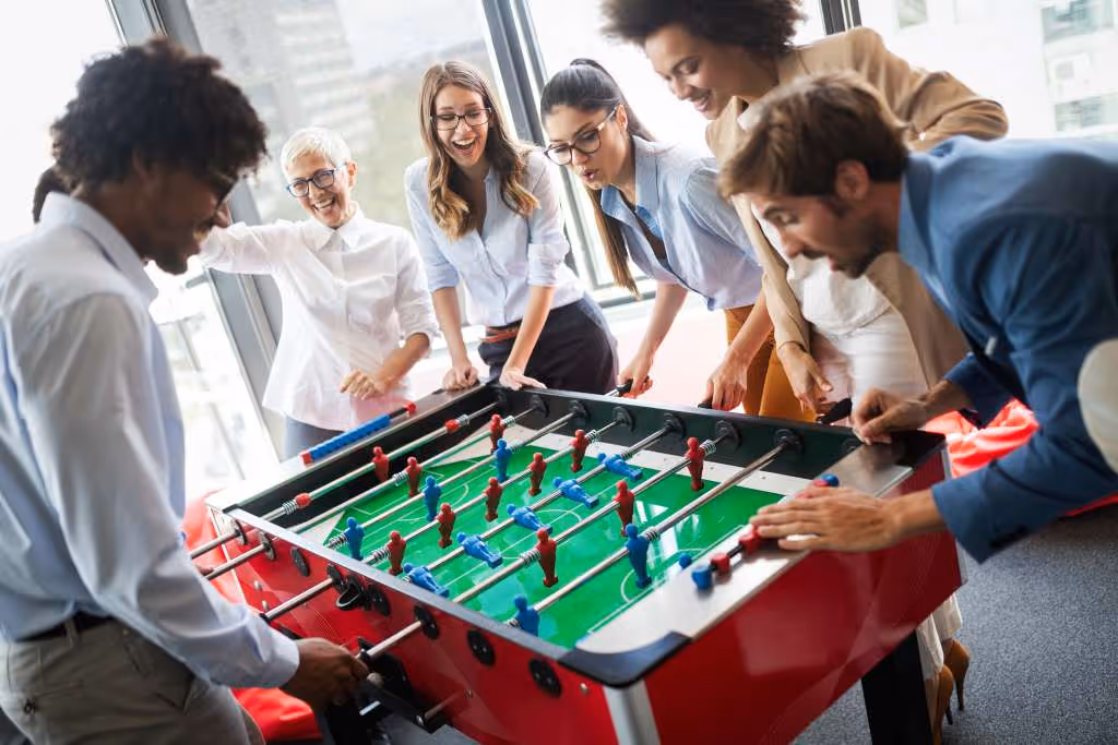 Team of employees playing table football together in the office, engaging in a fun group activity to reduce stress and build connections