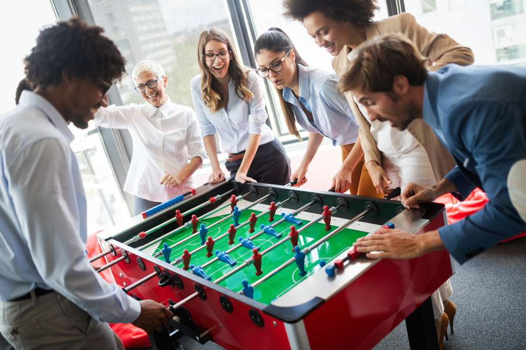 Team of employees playing table football together in the office, engaging in a fun group activity to reduce stress and build connections