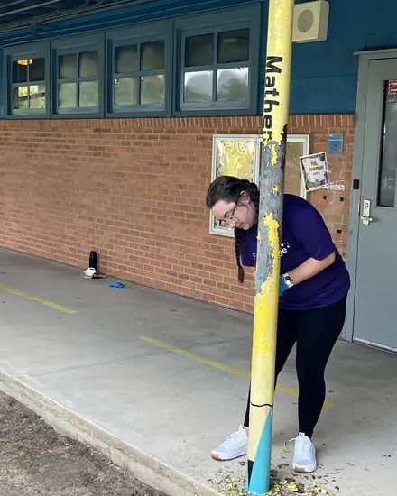 A volunteer scraping and prepping a schoolyard post