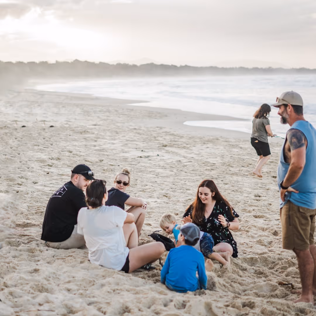 A family sitting on the beach at sun set playing in the sand.