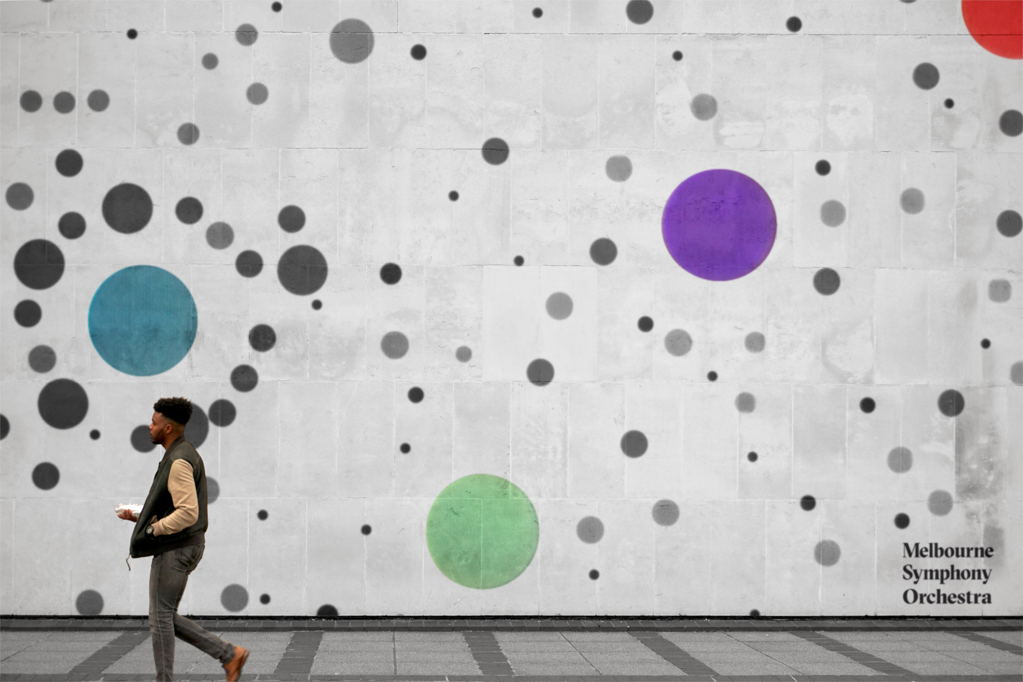 A man walking past a wall with a coloured sound visualisation projected on it