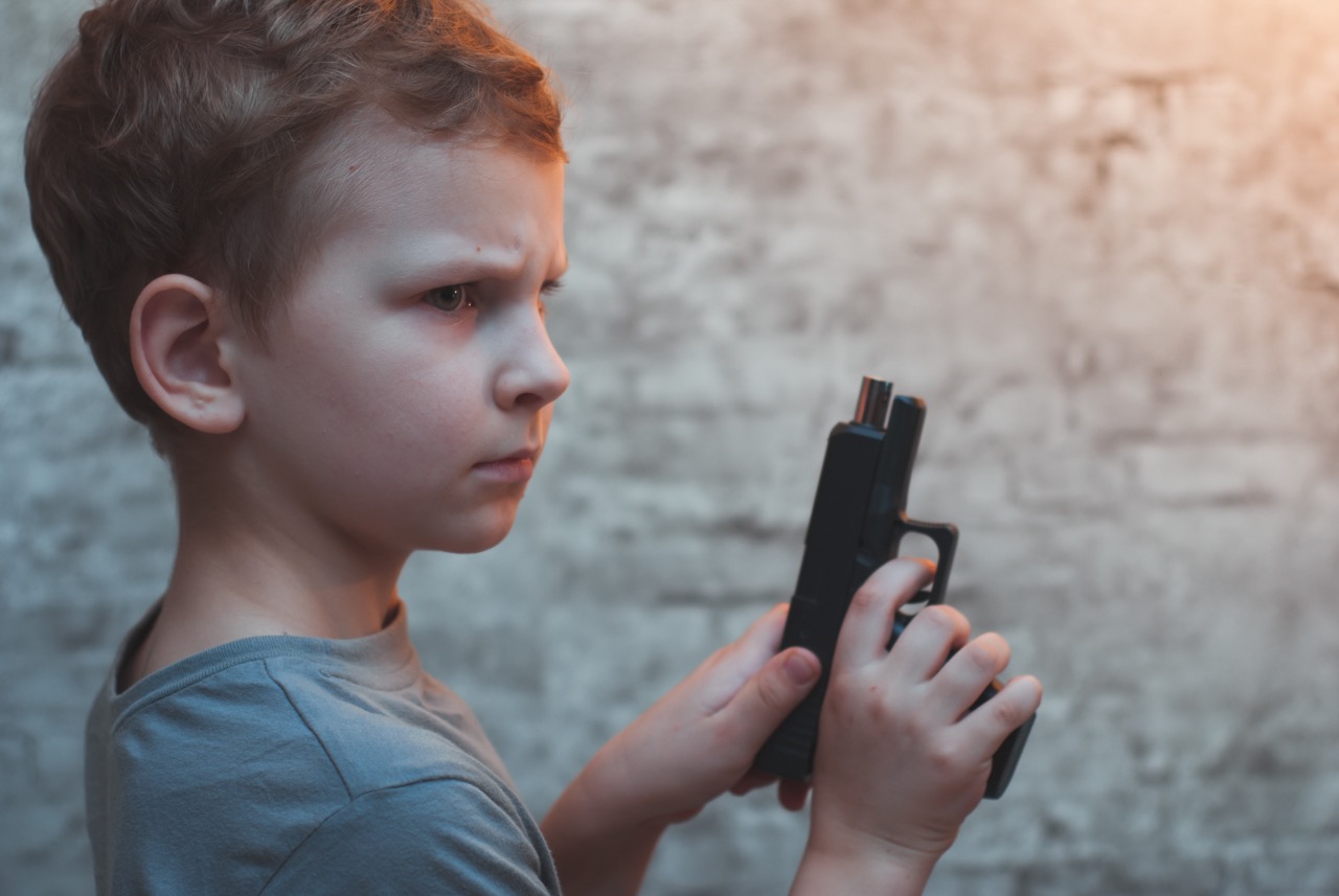 a white young boy holds a firearm looking angry