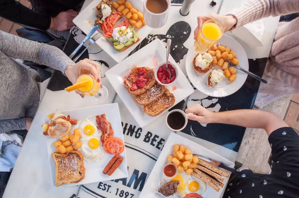 Overhead view of four people eating breakfast with eggs, toast, tater tots, coffee, and juice.