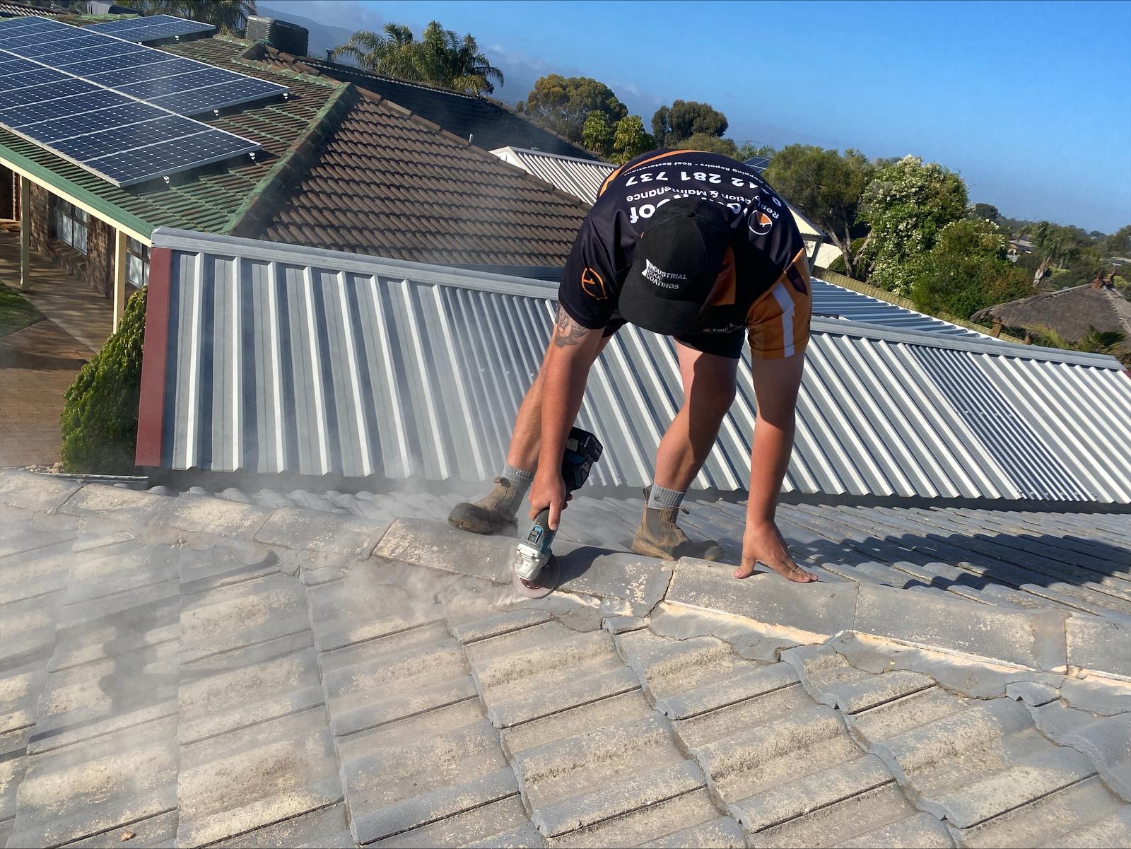 Your Roof Restoration crew cutting tiles on an Adelaide roof, with hills and solar panels behind.