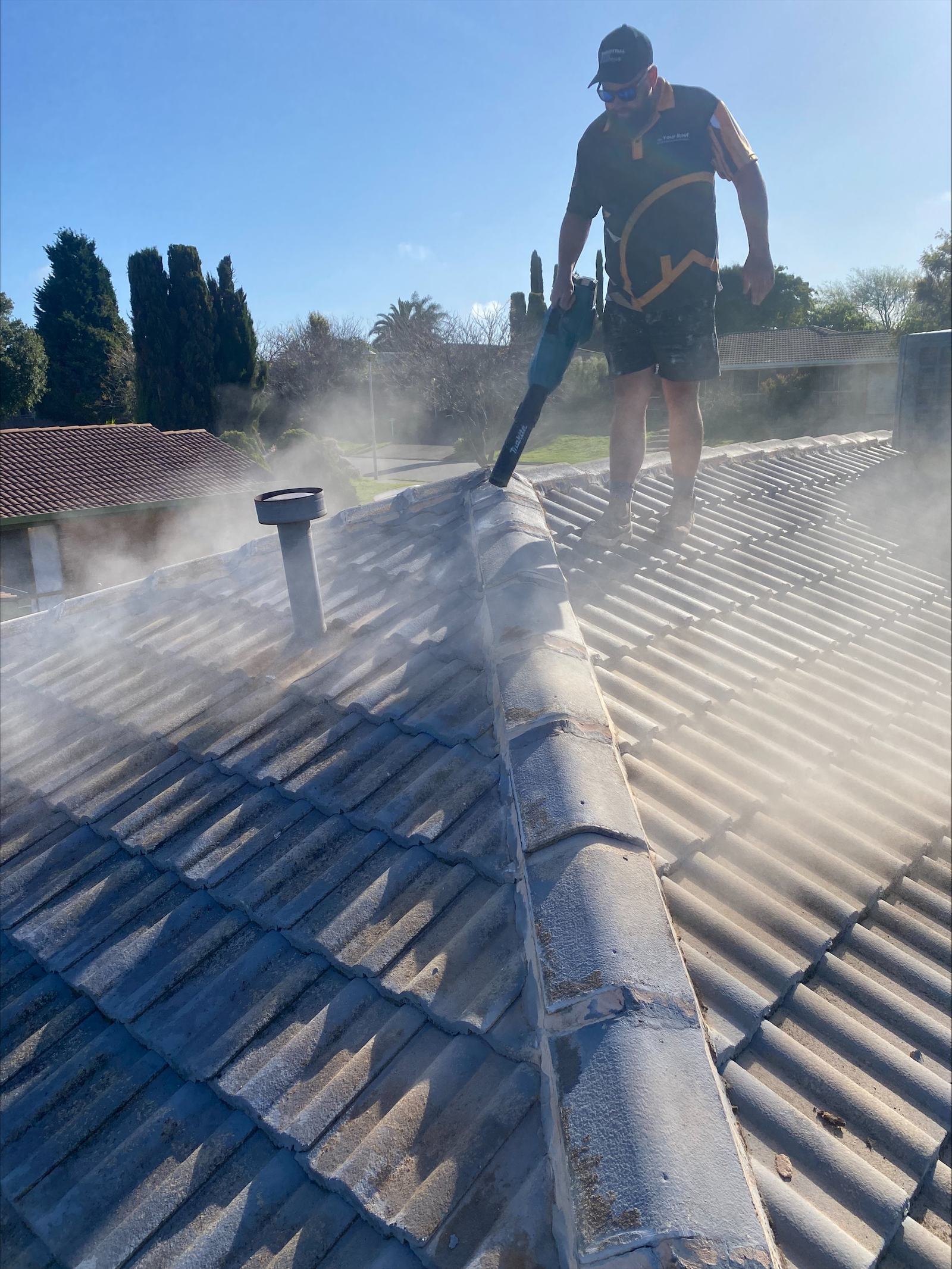 Your Roof Restoration crew member on a tiled Adelaide roof, clearing the ridge beside an existing roof vent.