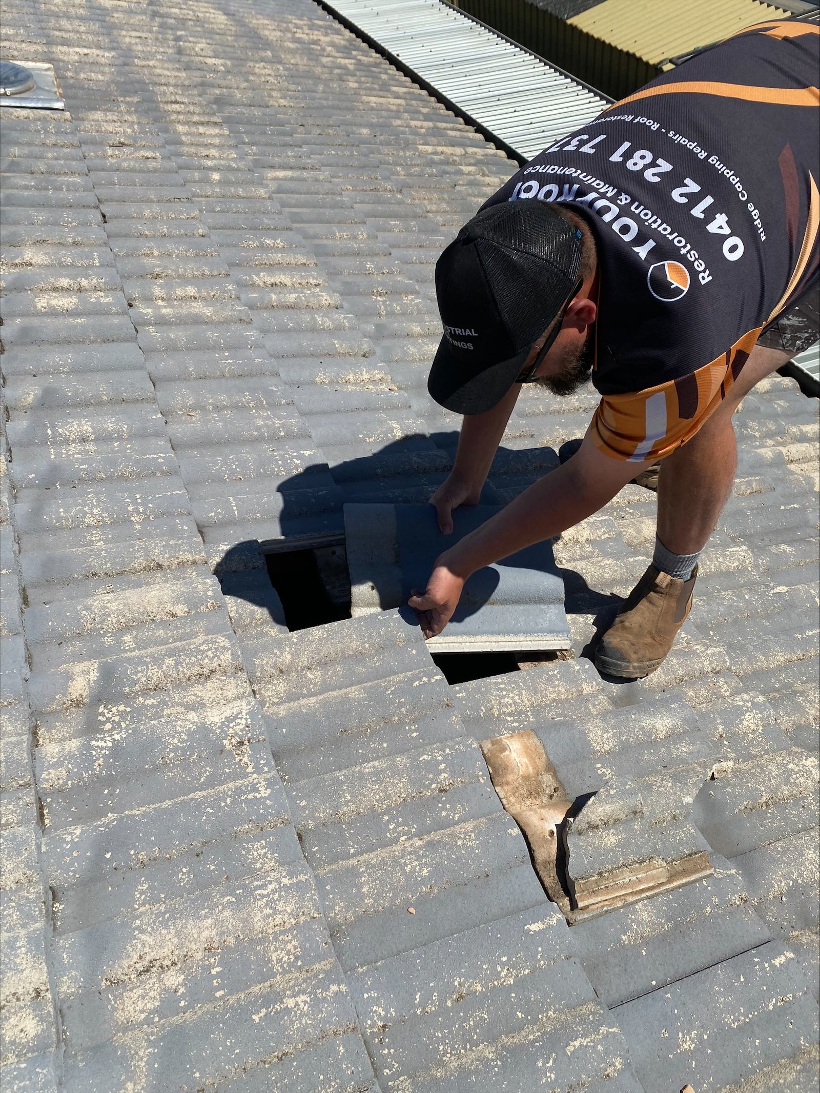 A Your Roof Restoration roofer opening tiles on a roof, with a small roof vent visible up the slope.