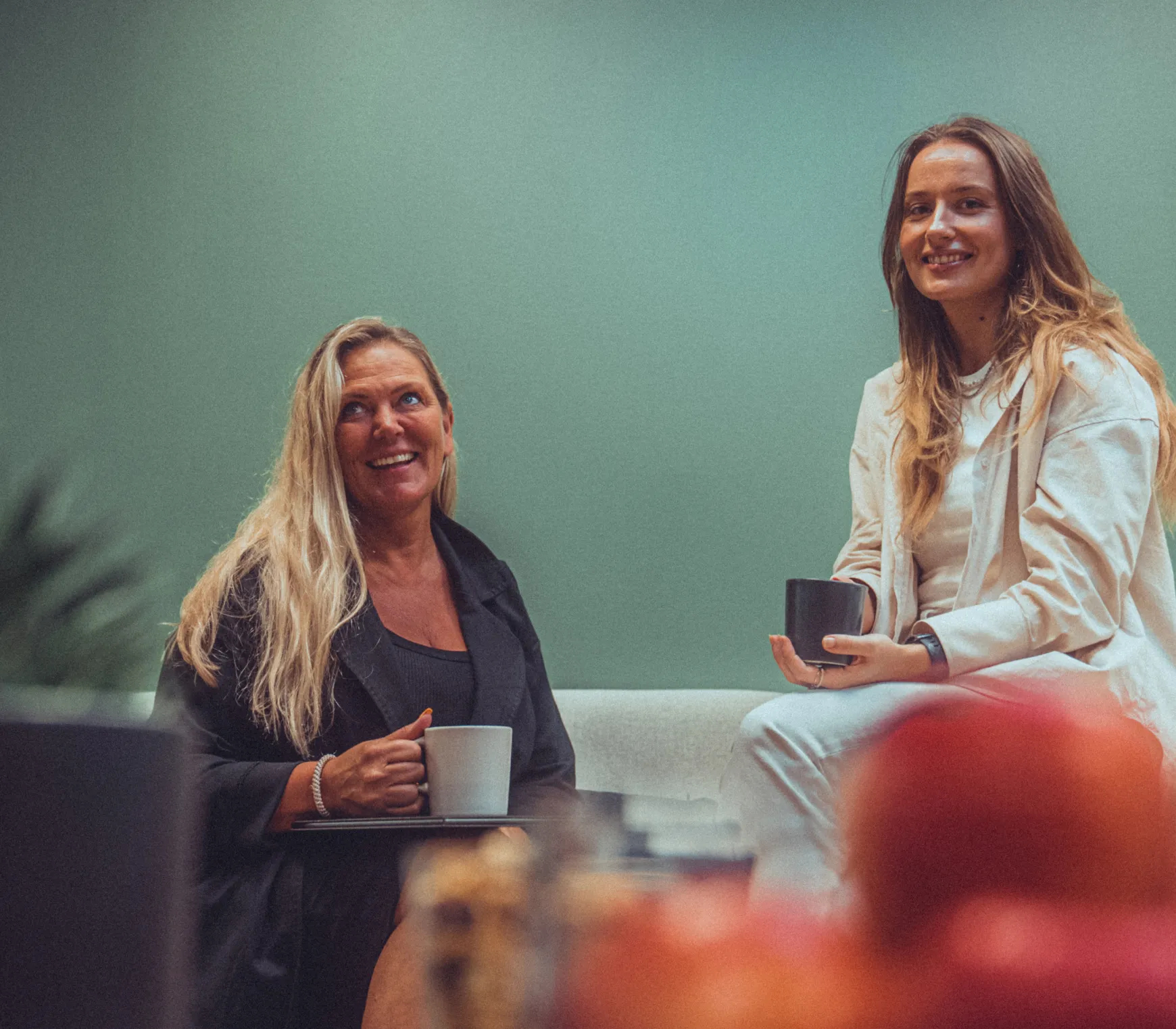 Alexandra og Monika som sitter i en sofa og smiler til kamera