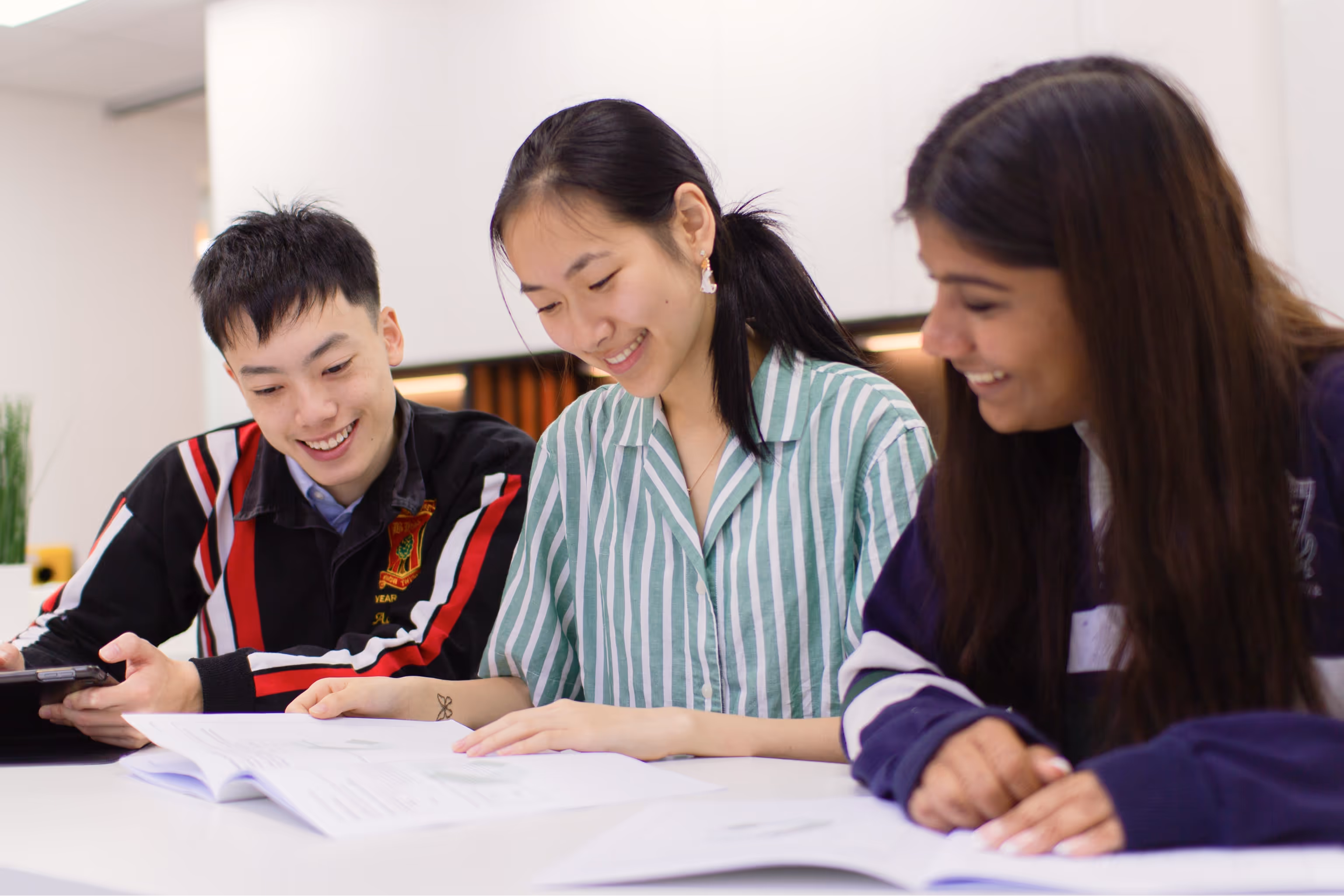 Three Cognito students sitting at a table, smiling and studying together with open books and a tablet.