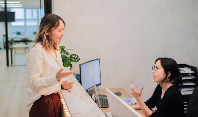 Two women having a discussion across a Cognito reception desk with a computer and office supplies.