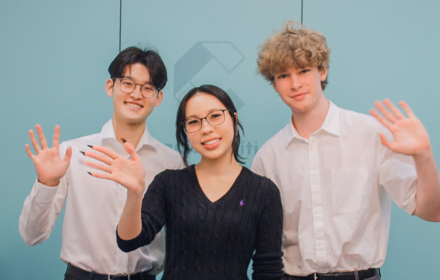 Three young Cognito staff smiling and waving at the camera against a teal background.