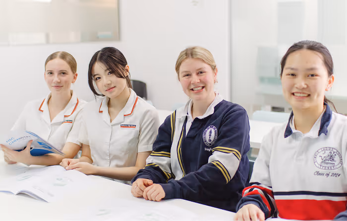 Four high school students sitting at a table in a bright Cognito classroom, smiling and facing the camera.