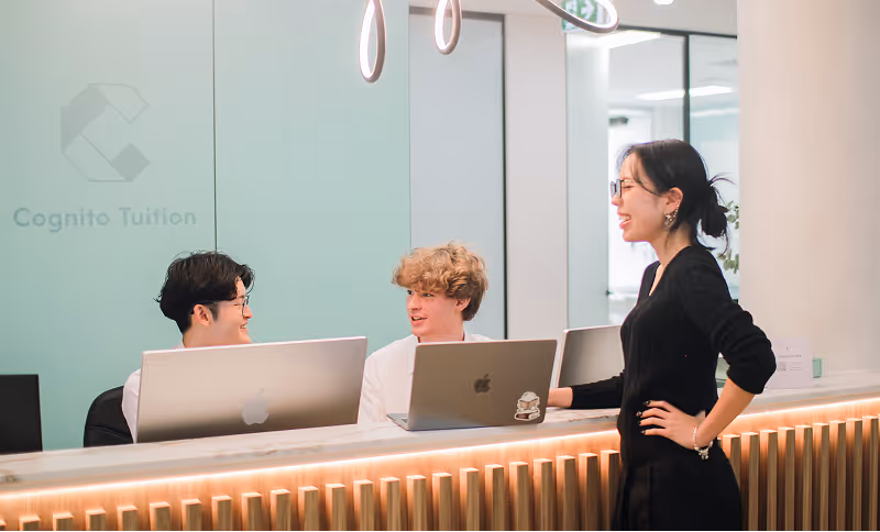 Three smiling Cognito staff at a reception desk with computers, one standing and two seated, engaged in conversation.