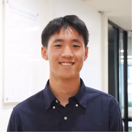 Young man with short black hair wearing a dark blue collared shirt smiling indoors.