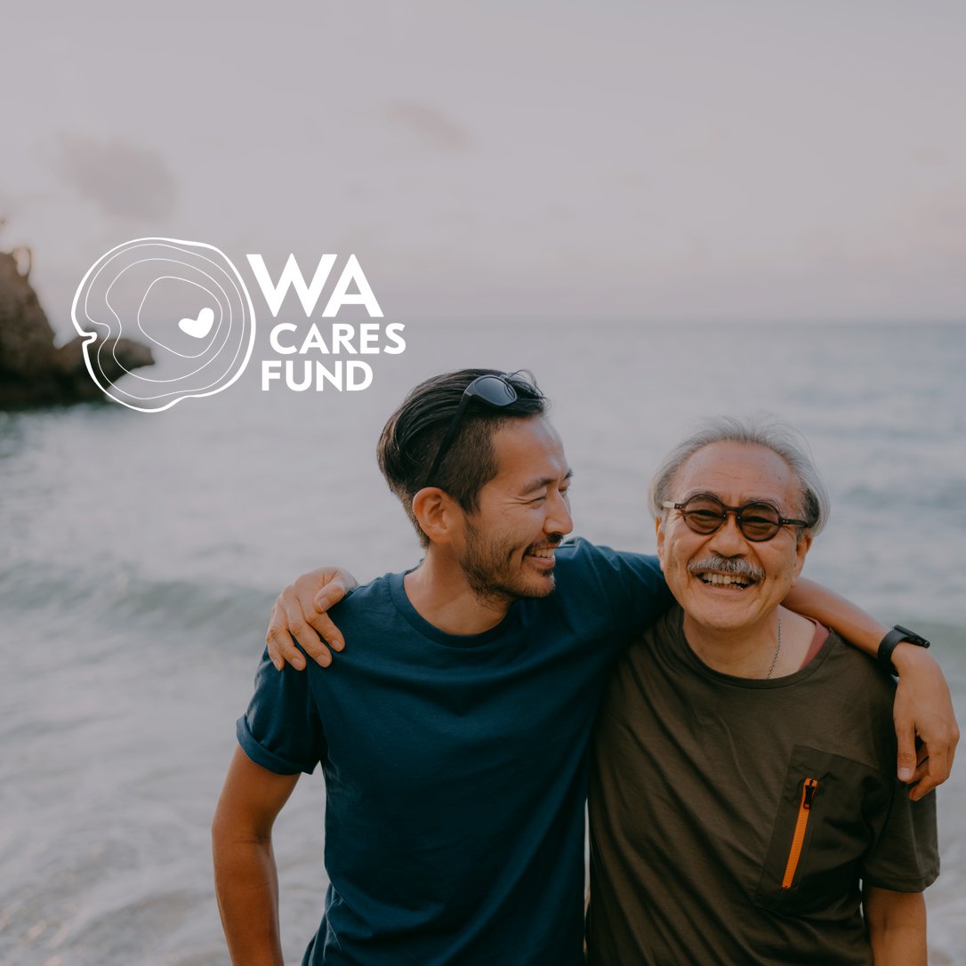 An adult son with his arm around his father at the beach, with the WA Cares Fund logo