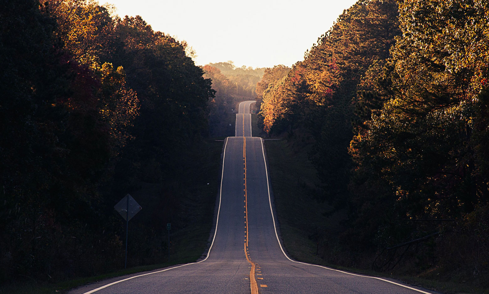 Hilly road vanishing over the horizon at sunset