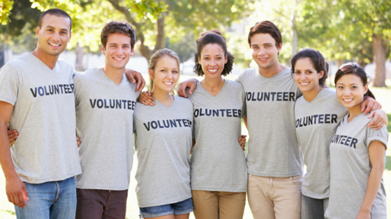 A group of smiling volunteers standing together outdoors, wearing matching gray T-shirts with the word âVOLUNTEERâ printed on them.