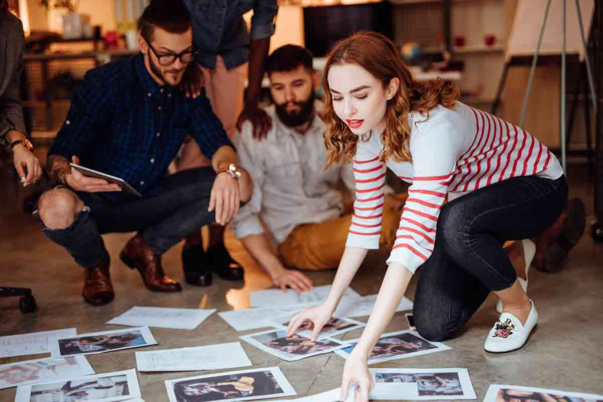 Employees participating in an office treasure hunt, examining printed clues and photos spread across the floor as they work together to solve the challenge.
