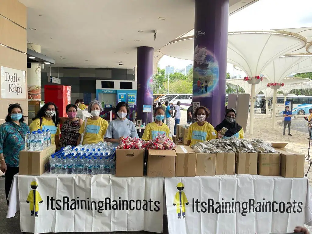 Volunteers from ItsRainingRaincoats distributing food and water to migrant workers in Singapore, promoting community support and inclusion.
