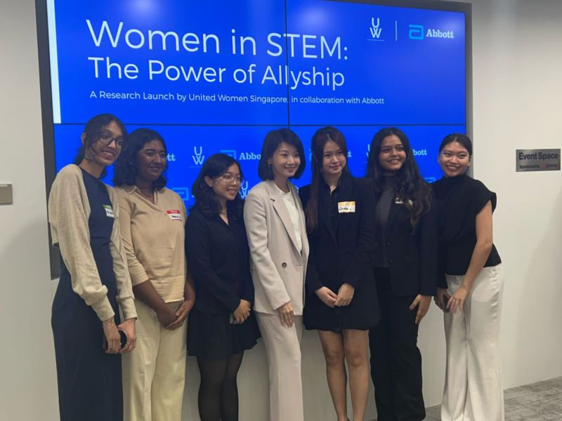 Group of women standing together at a Women in STEM event, posing in front of a screen highlighting allyship and collaboration.