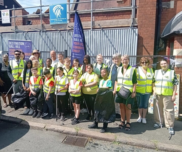 A group of volunteers wearing high-visibility vests pose on a street after a community cleanup, holding litter pickers and trash bags.