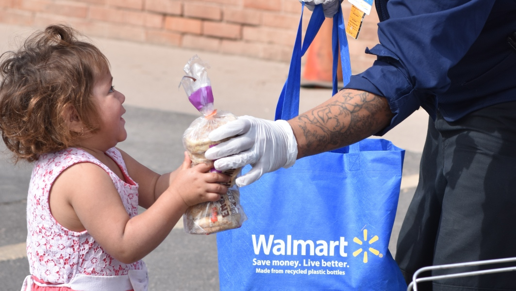 Walmart employee volunteer handing food to a child during a community outreach event