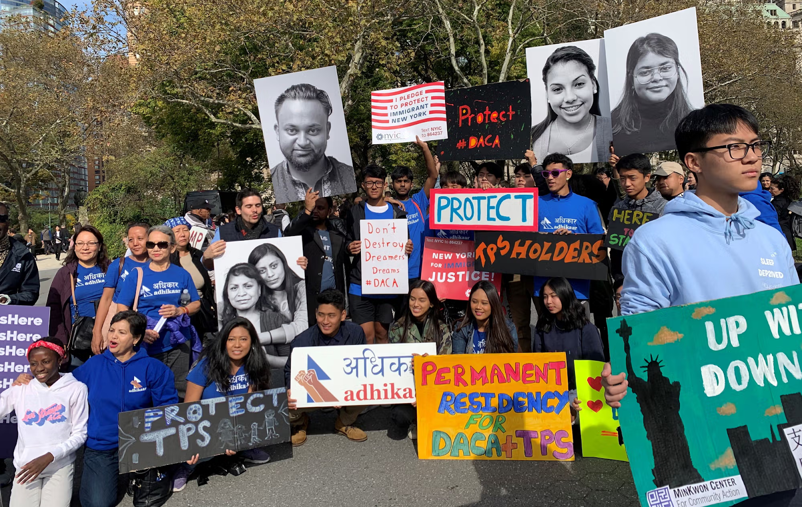 Community members and activists at a rally holding signs advocating for immigrant rights, DACA protection, and permanent residency
